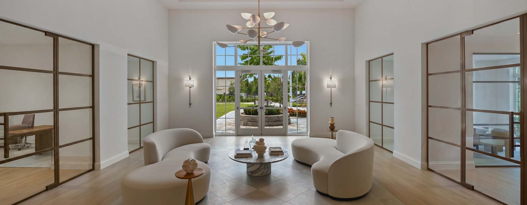 Double-height lobby with a sculptural chandelier, curved seating, and glass doors to the courtyard at Sereno