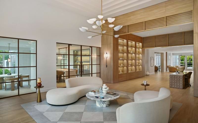 Leasing lounge with curved cream sofas, a marble coffee table, and backlit oak shelving at Sereno in Sunrise, FL