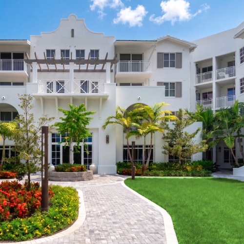 Landscaped courtyard with flowering garden beds and a paver walkway at Sereno in Sunrise, FL