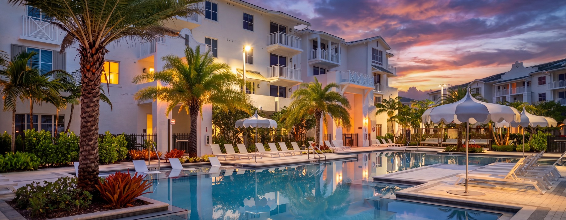 Resort-style swimming pool at sunset at Sereno apartments in Sunrise, FL, with palms, umbrellas, and lounge seating