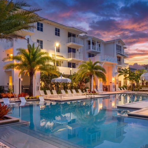 Resort-style swimming pool at sunset at Sereno apartments in Sunrise, FL, with palms, umbrellas, and lounge seating
