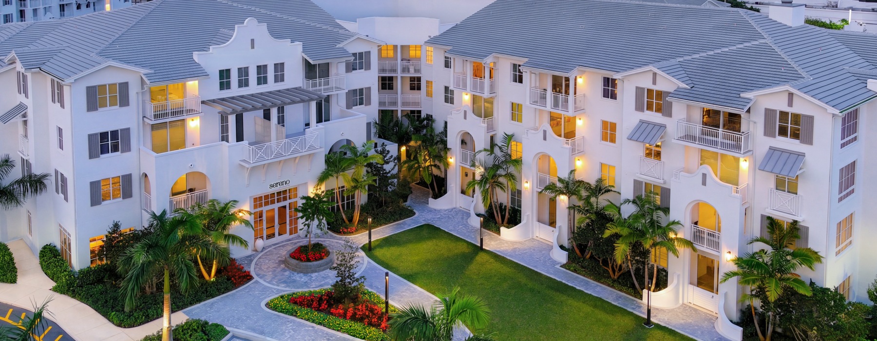 Aerial view of Sereno luxury apartments in Sunrise, FL at dusk with a paver courtyard and palm-lined entrance