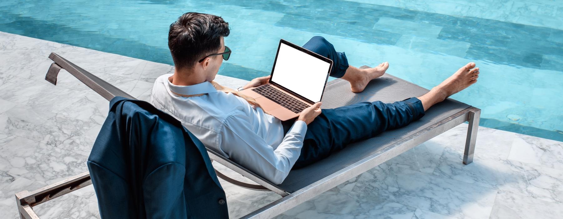 a man lying on a chair with a laptop by a pool